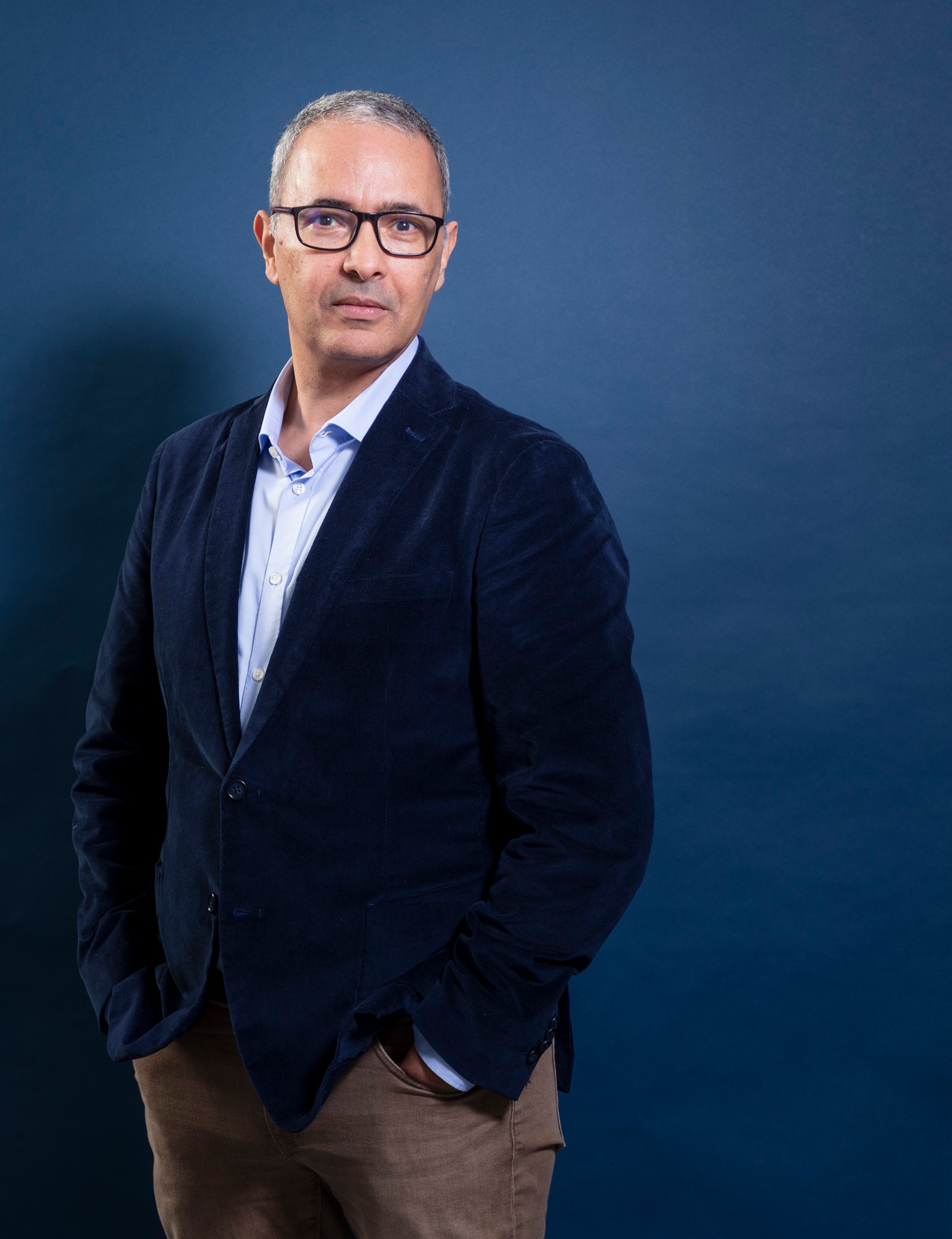 Man i 50–60-årsåldern med kort grått hår och glasögon, i blå kavaj mot blå bakgrund.