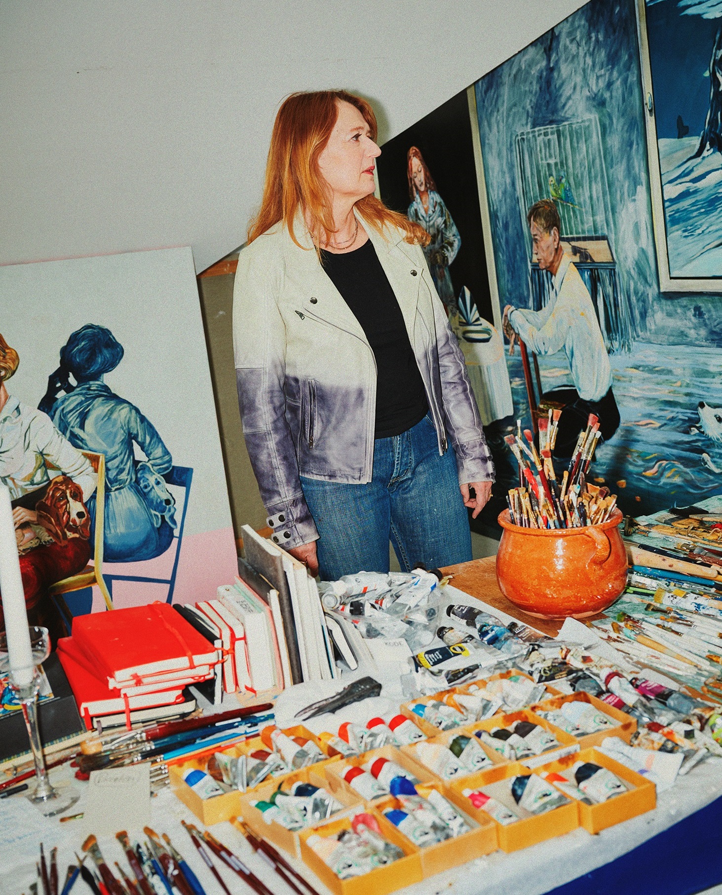 Konstnären Meta Isæus-Berlin står vid bord med penslar, färgtuber och målningar i en ateljé.