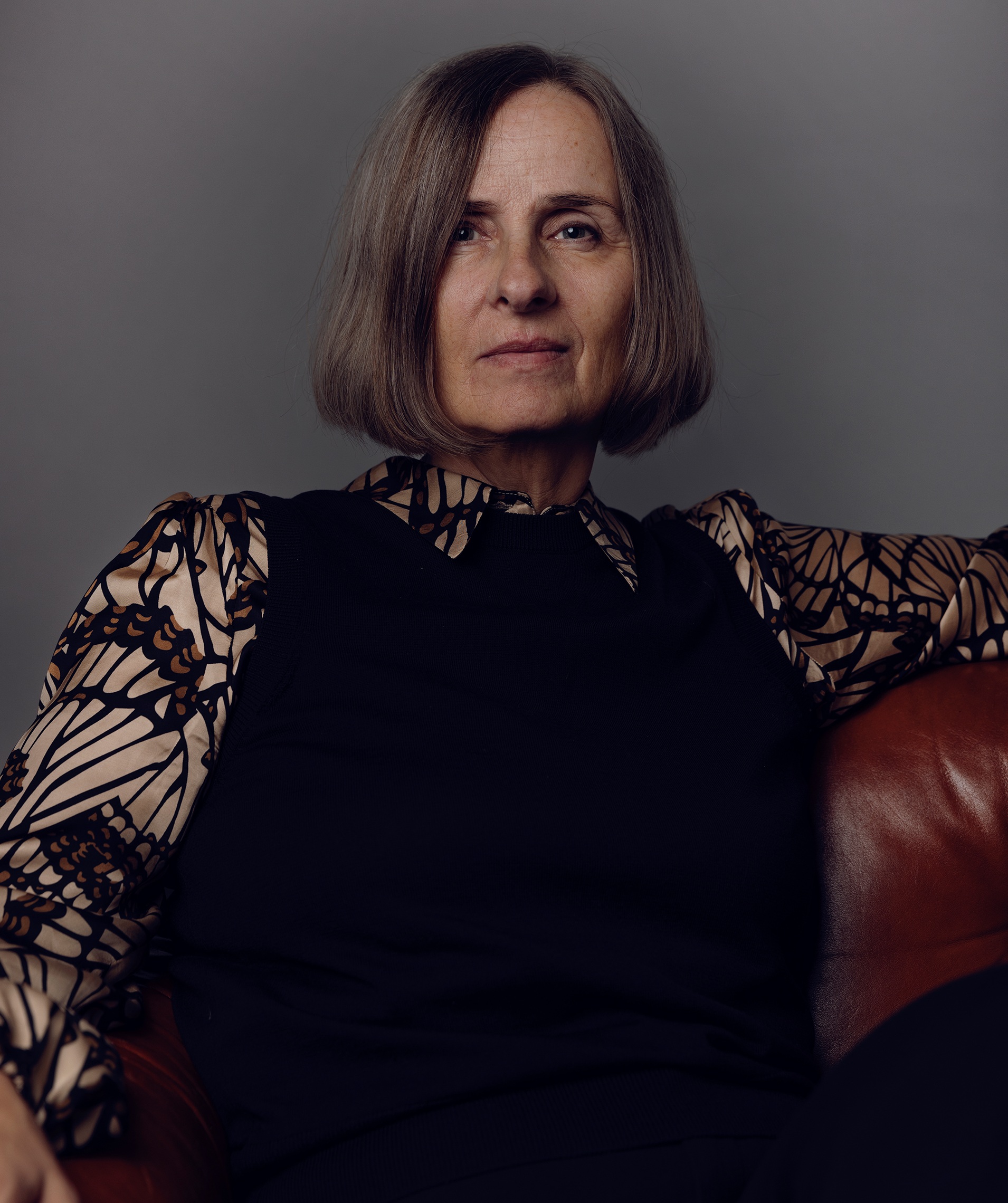 Susanna Alakoski sitter i en läderfåtölj med armarna utsträckta i ett självsäkert och balanserat porträtt med dämpade färger.