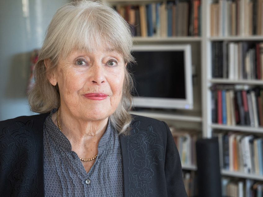 Porträttfoto på författaren Agneta Pleijel med en bokhylla full av böcker bakom sig.