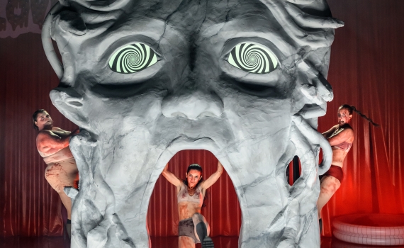 Ett stort Medusa-liknande huvud på scen och fem skådespelare runt huvudet. 