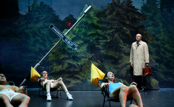 Tre personer i badkläder ligger i solstolar, en man i trenchcoat står bredvid en lutande vägskylt.