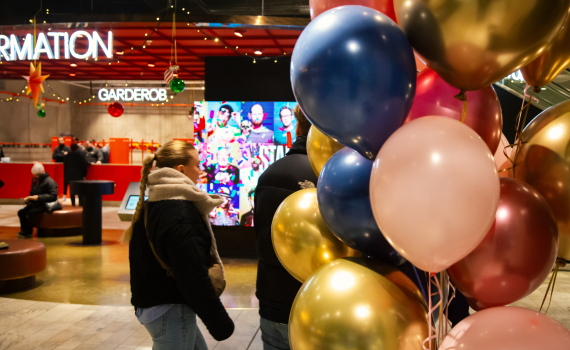 Kvinna passerar ballongkluster vid informationsdisk med juldekorationer i ett offentligt utrymme.