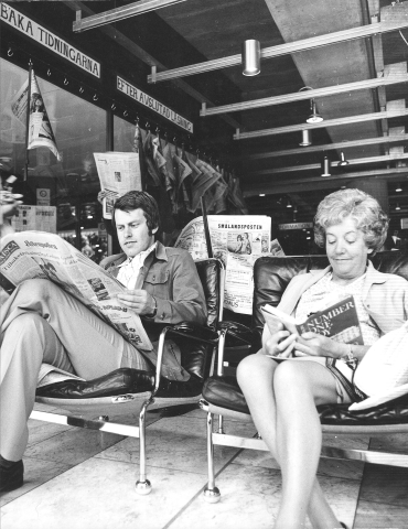 Det är 70-tal, en man och en kvinna sitter i varsin fåtölj i Kulturhuset och läser böcker och tidningar. 