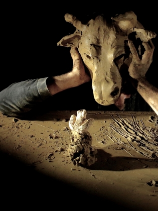 Två händer håller upp ett stort giraffhuvud av lera. 