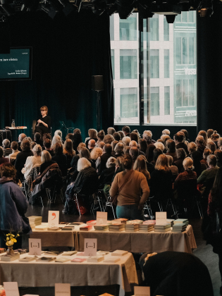 En engagerad publik samlad i en inspirerande litteraturmiljö. Samtal på en scen, omgivet av böcker.