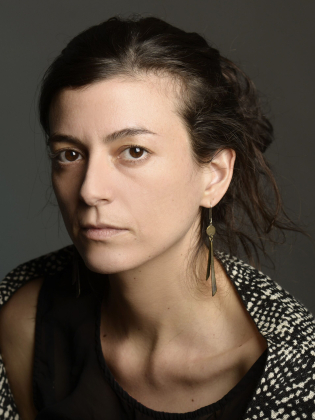 Kvinna i 30–40-årsåldern med långt mörkt hår, lång örhänge och svart topp, ser rakt mot kameran.