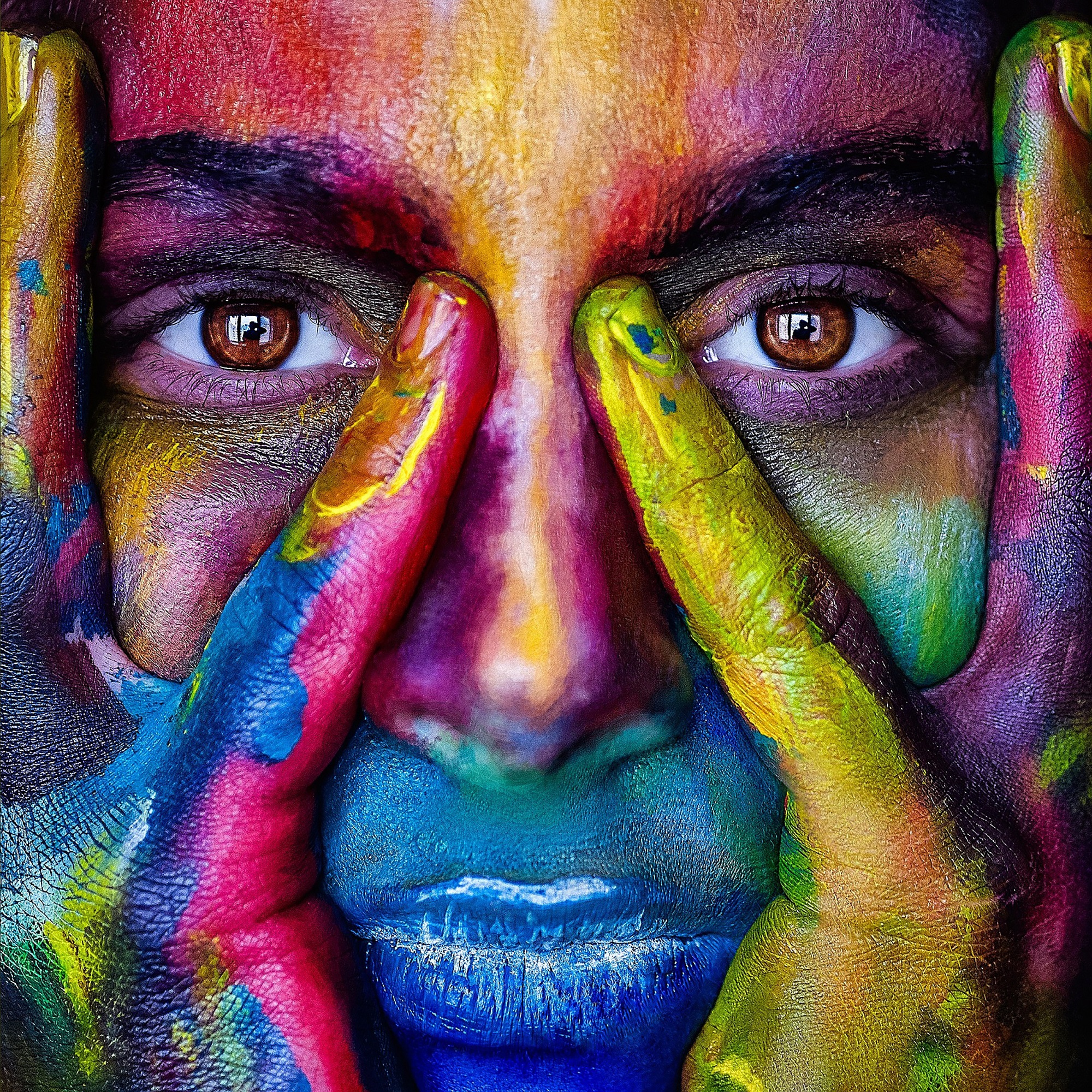 Ett ansikte och ett par händer målade i olika färger. 
