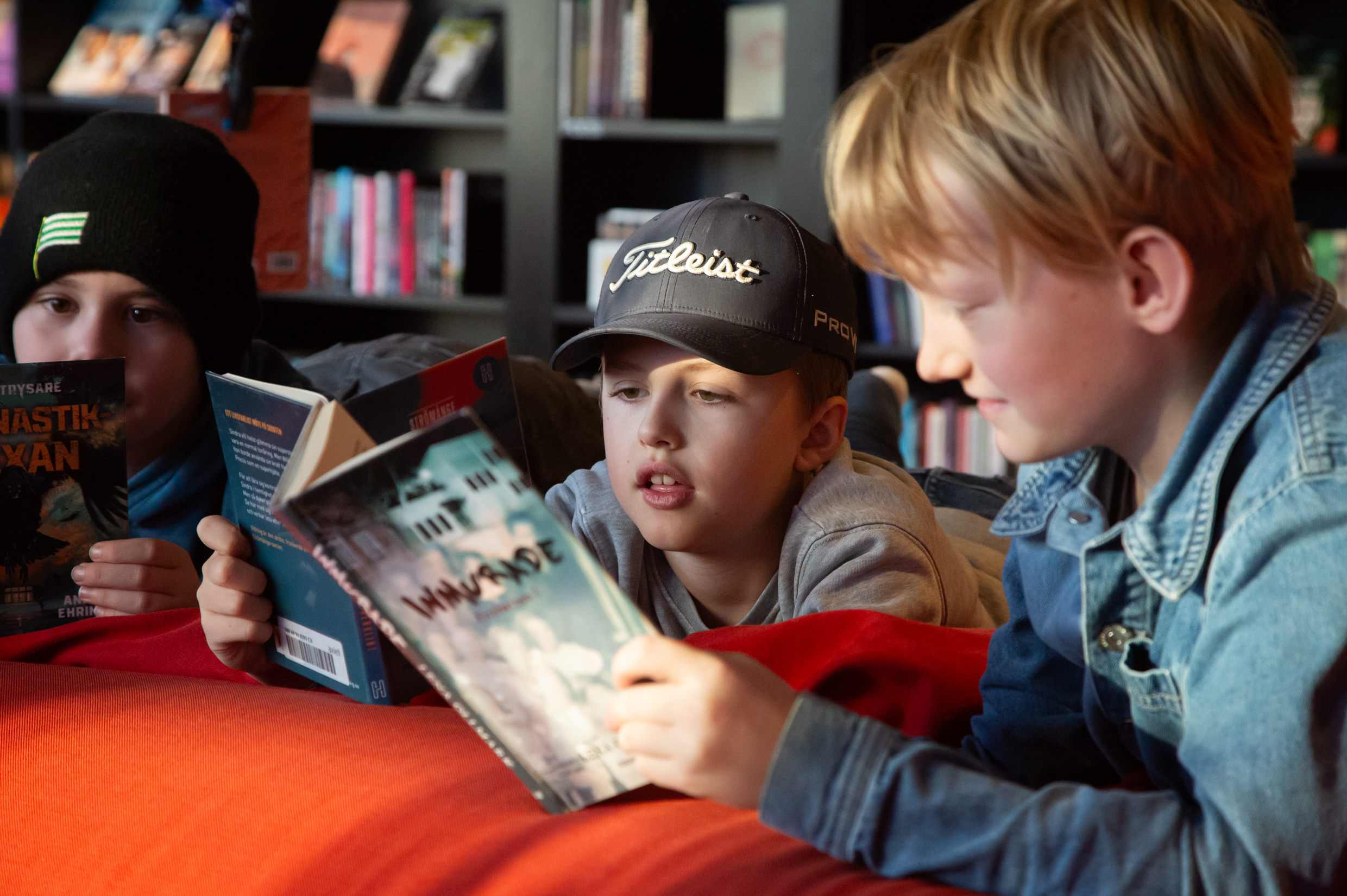 Tre barn läser varsin bok i biblioteket