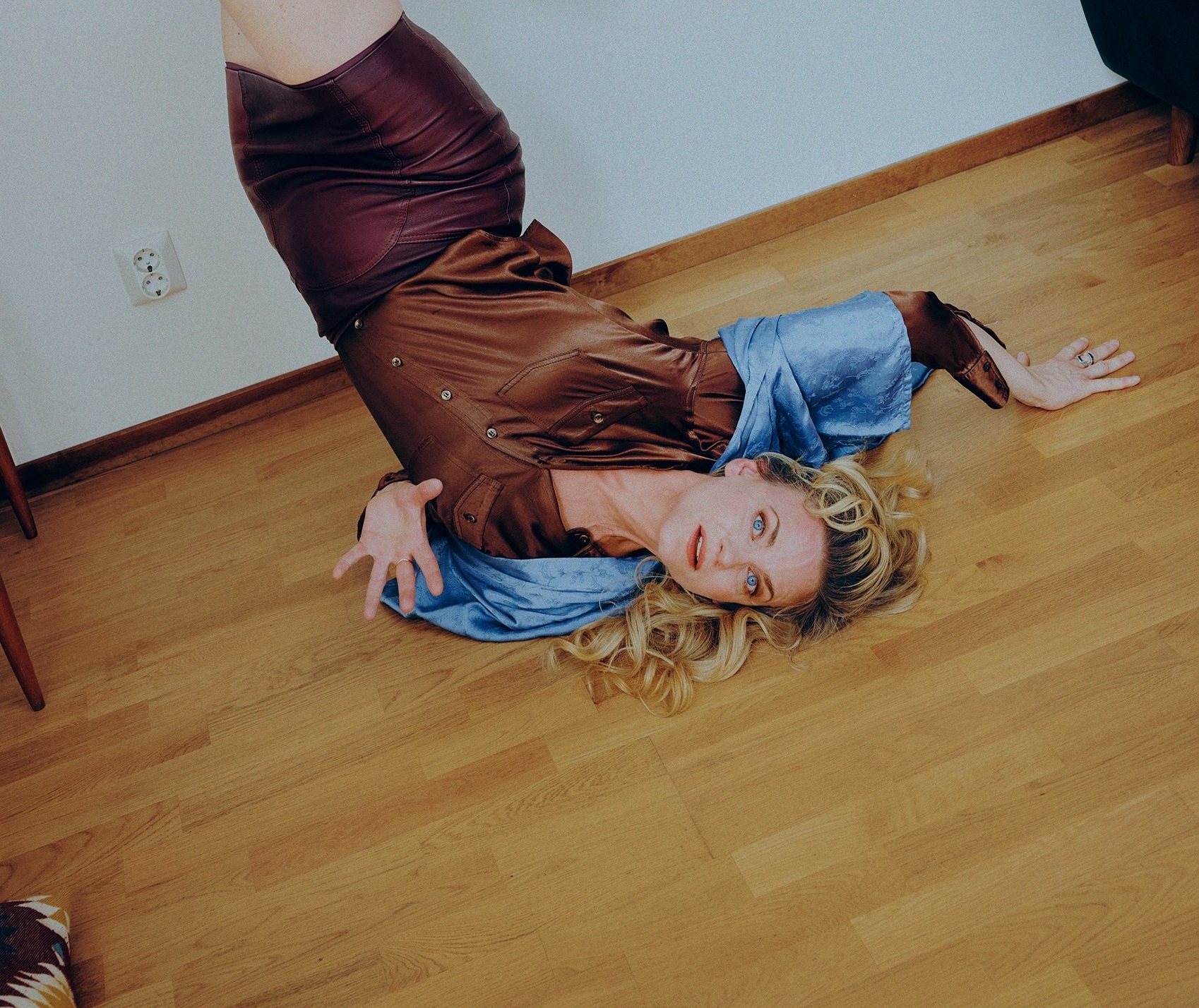 Kvinna i 30–40-årsåldern ligger på golvet med benen upp mot väggen, iklädd brun klänning med blå detaljer.