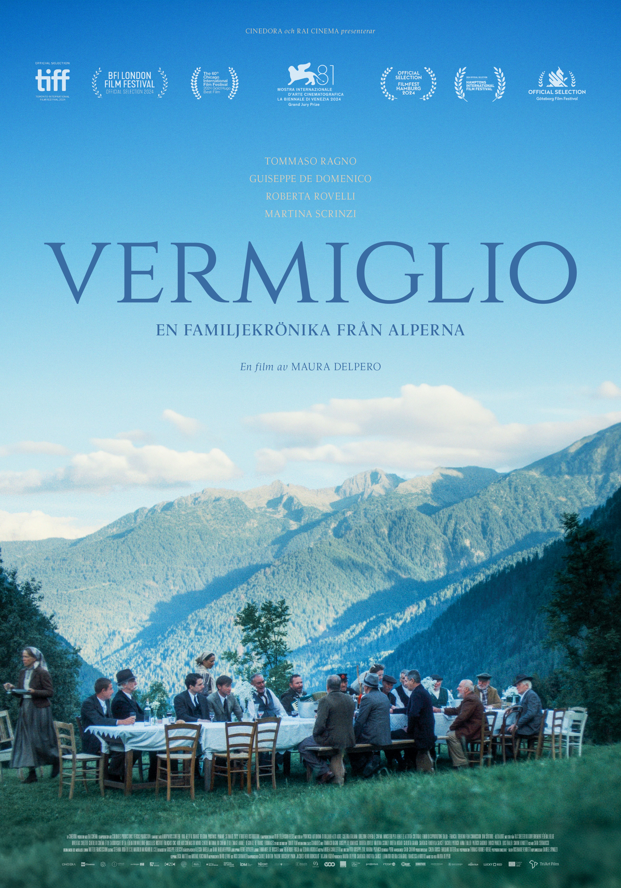 En grupp människor sitter vid ett dukat bord i ett alplandskap.