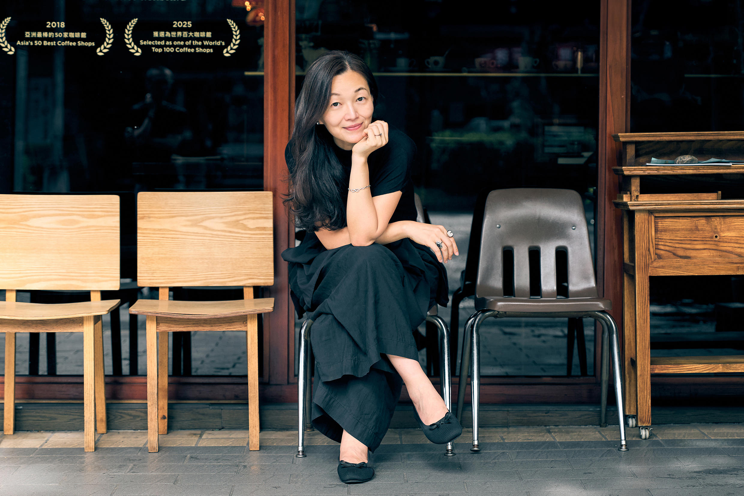 Lee Chia-Ying sitter utanför ett café i ett avslappnat och varmt porträtt där miljön ger bilden en vardaglig och inbjudande ton.