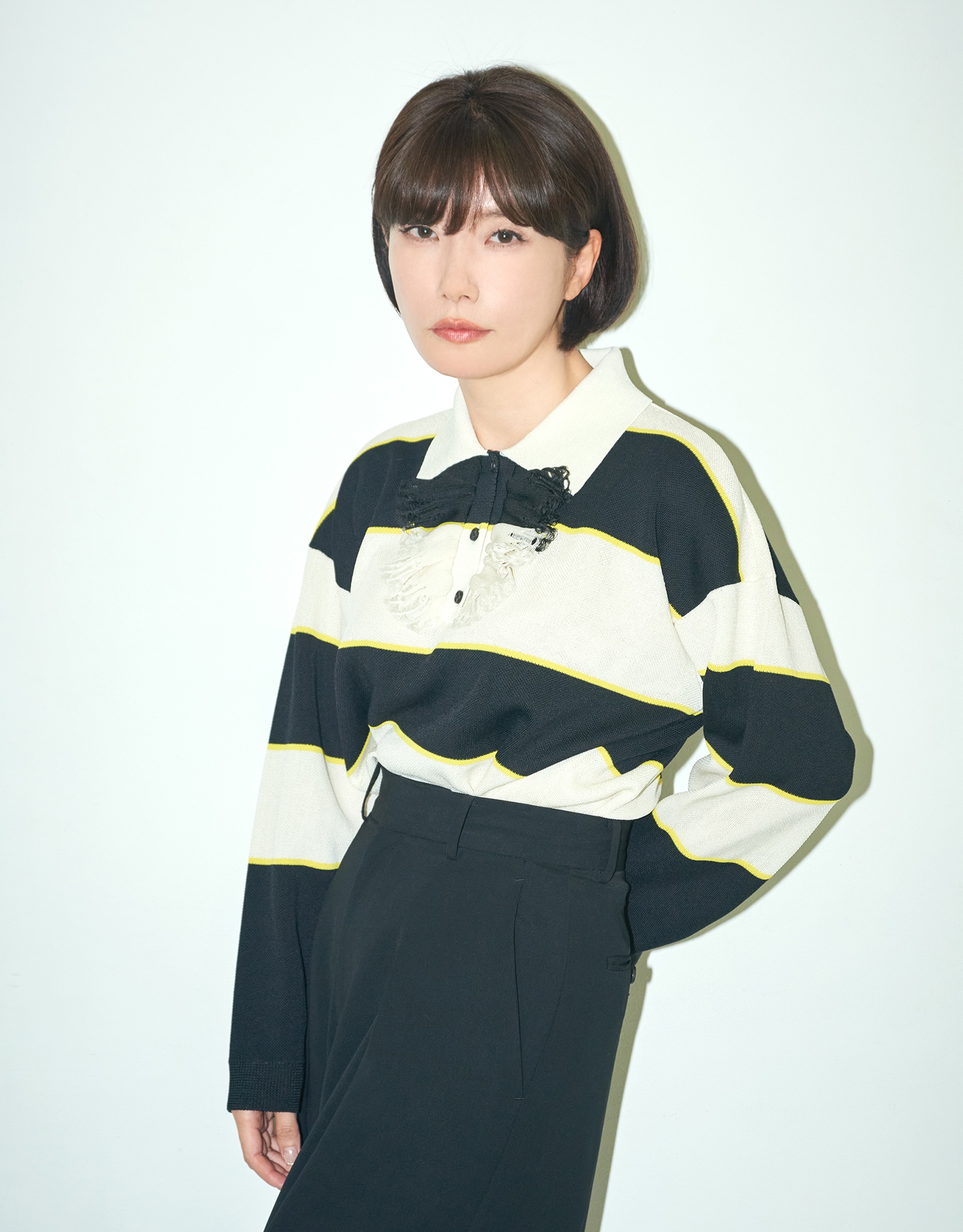 Mieko Kawakami står mot en ljus bakgrund i ett minimalistiskt porträtt med tydliga kontraster och ett lugnt, fokuserat uttryck.