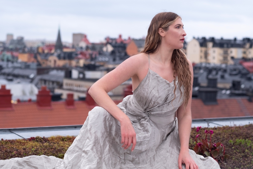 Operasångaren Maja Frydén i en ljusgrå klänning med en stadssiluett i bakgrunden