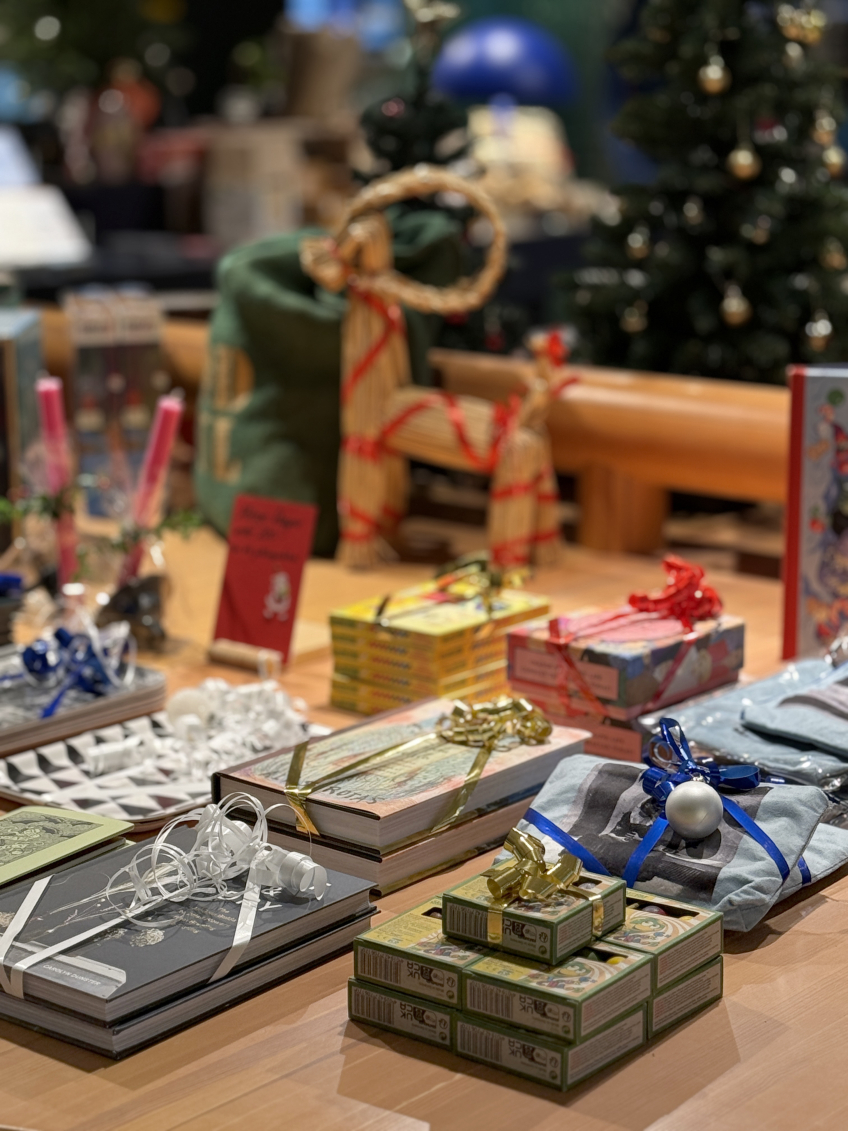 Närbild på juldekorerat bord med inslagna böcker, askar och halmbock framför julgran.