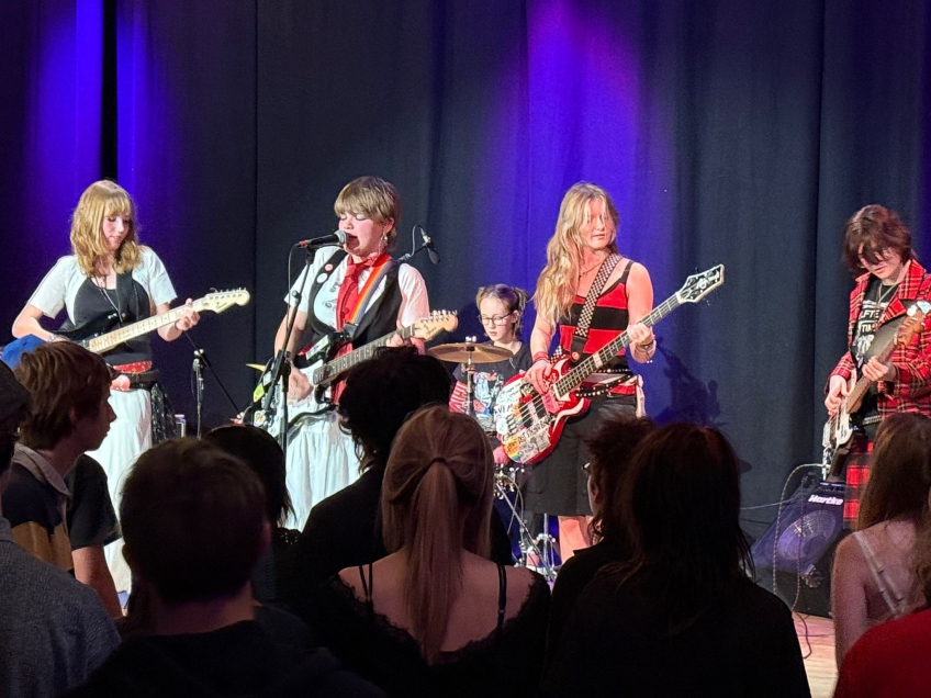 Fem kvinnor spelar elinstrument och trummor på scen inför en publik.