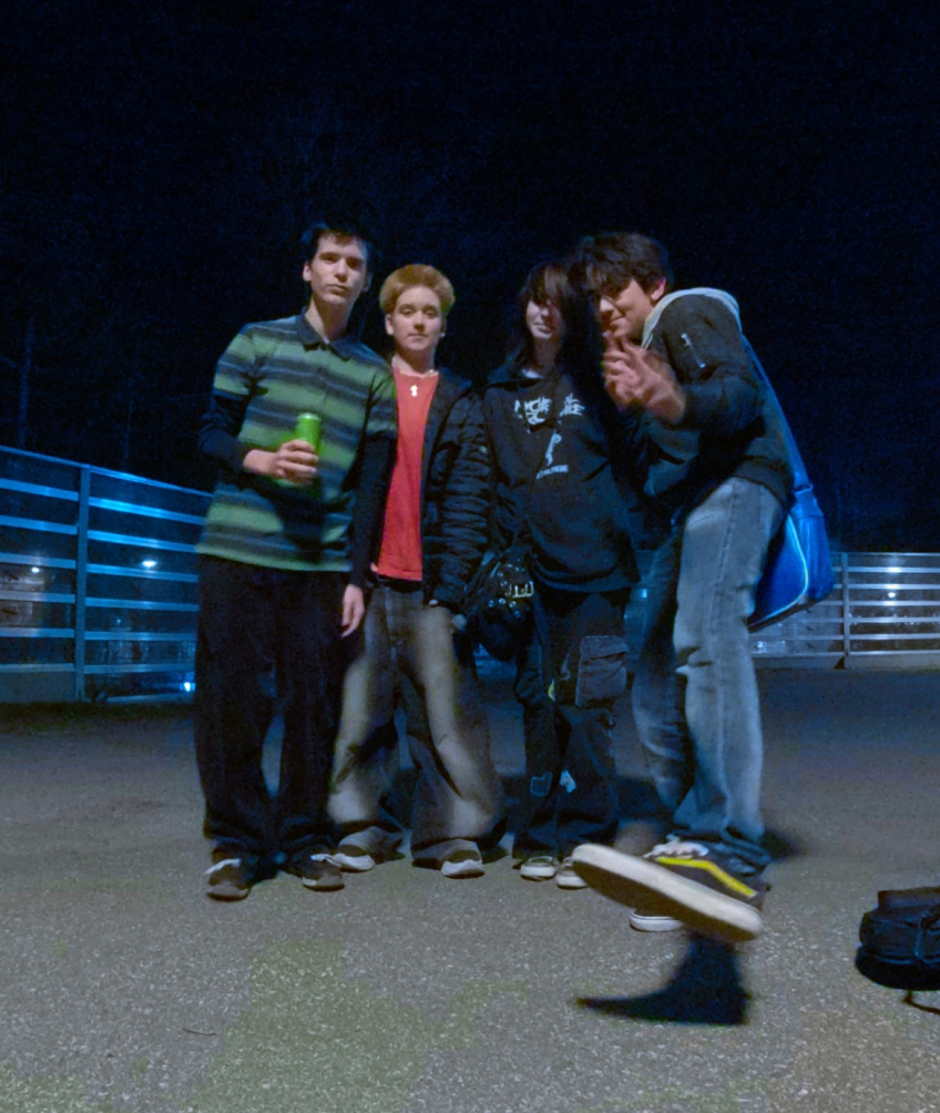 Fyra tonårspojkar poserar utomhus på kvällen, en av dem i luften mitt i ett hopp.