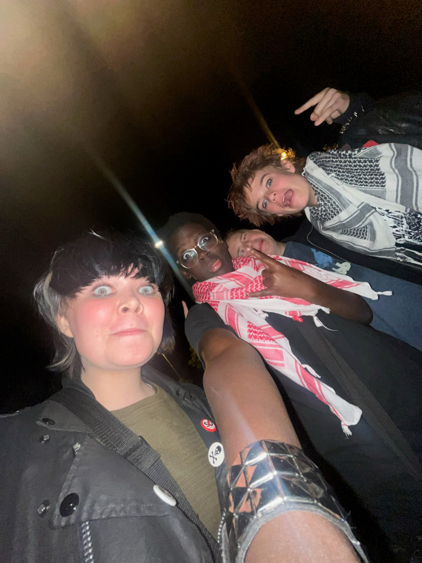 Fyra unga personer poserar för en selfie i mörker, två bär keffiyeh-sjalar och en har nitar på jackan.