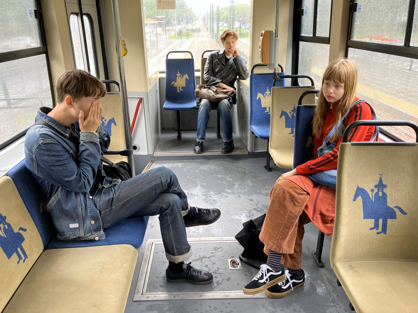 Tre unga personer sitter utspridda i en spårvagn, två framåtvända och en längst bak.