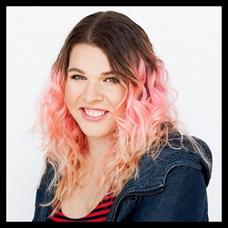 En person med rosa tonat hår som ler, fotograferad mot en ljus, ren bakgrund.