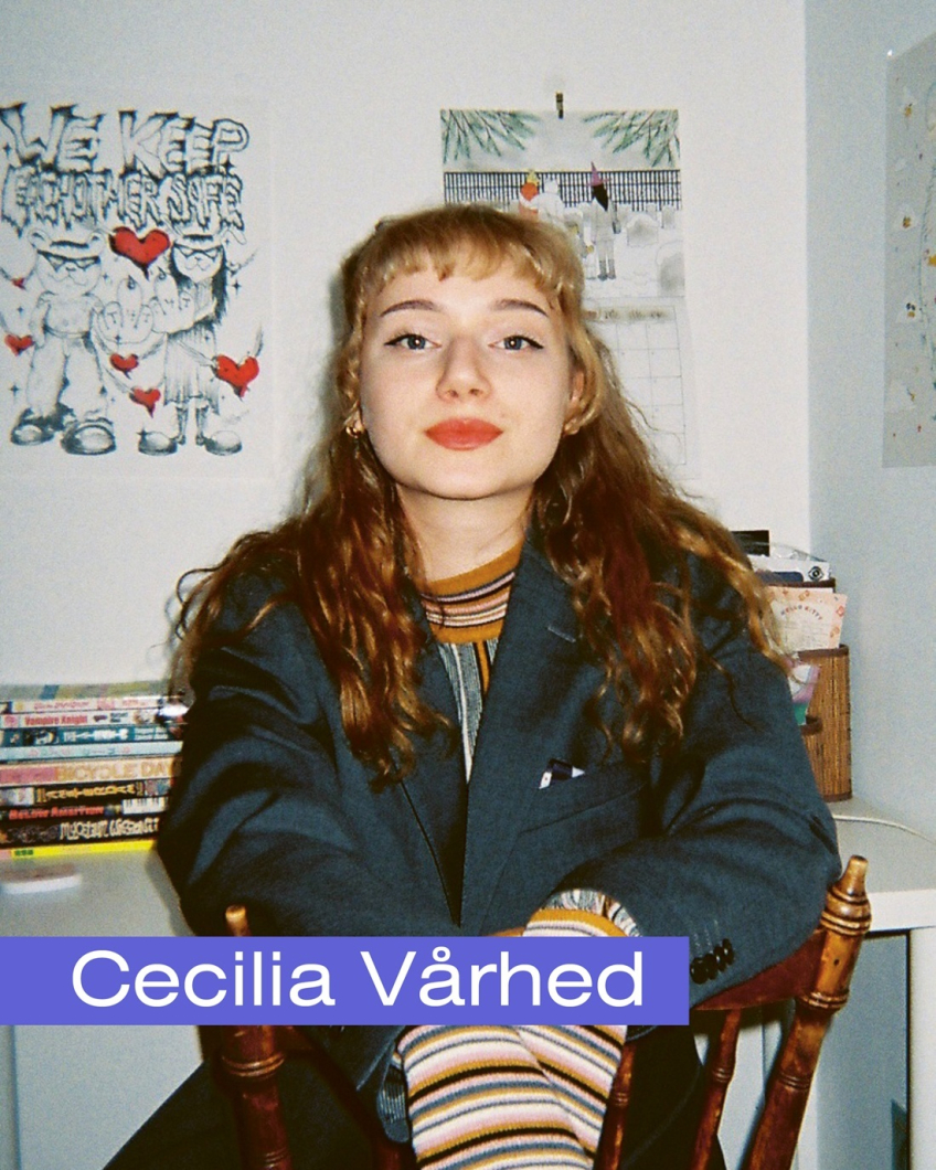 Porträtt av en kvinna sittande inomhus vid ett skrivbord, med böcker och teckningar i bakgrunden.