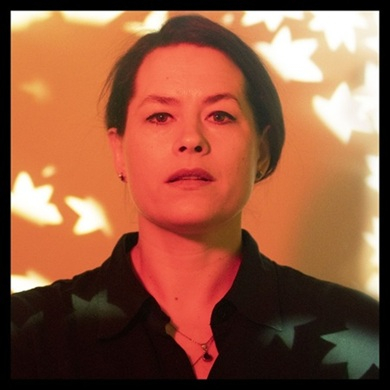 En person belyst i varmt röd-orange ljus med projicerade lövformer över ansiktet, vilket ger en konstnärlig och dramatisk känsla.