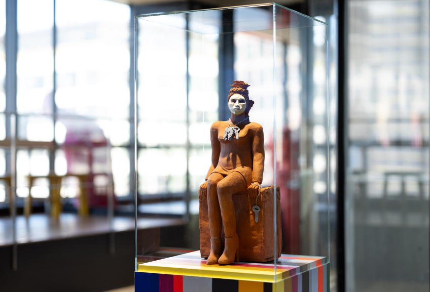 Närbild av keramisk figur med vitmålat ansikte och smycke, placerad i en glasmonter.