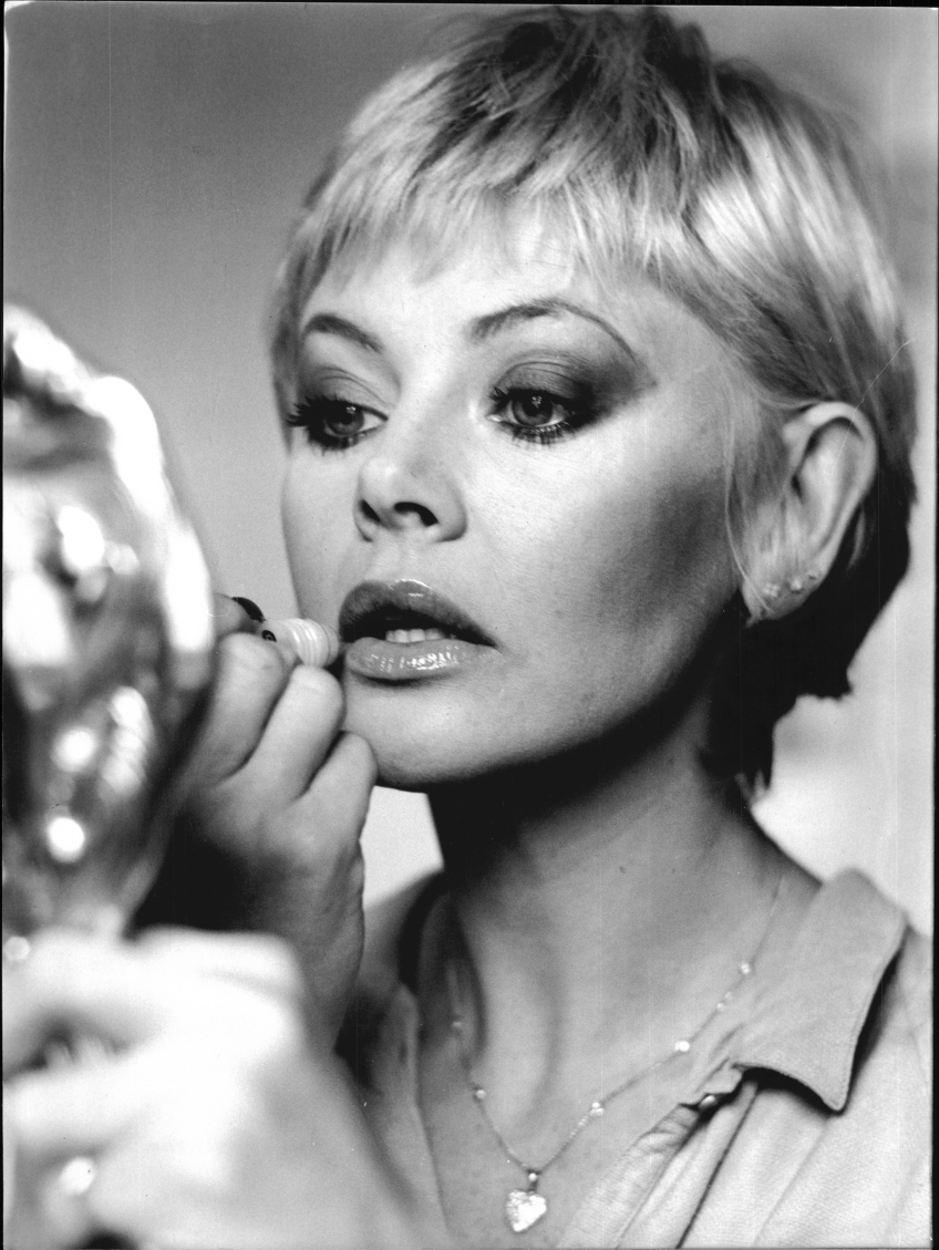 Britt Ekland som målar sina läppar med en handspegel framför sig