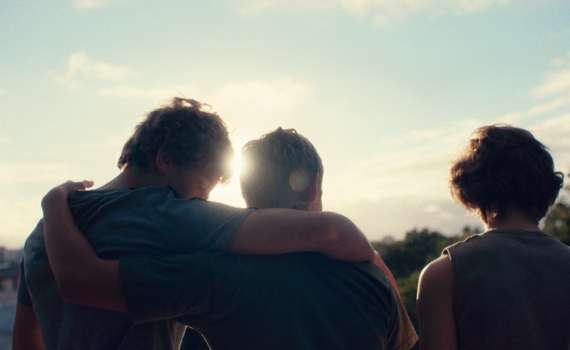 Tre unga killar i motljus håller om varandra i silhuett