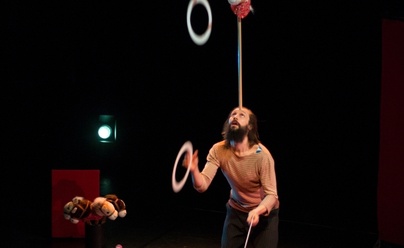 Cirkusartist som balanserar en käpphäst på huvudet och jonglerar ringar samtidigt