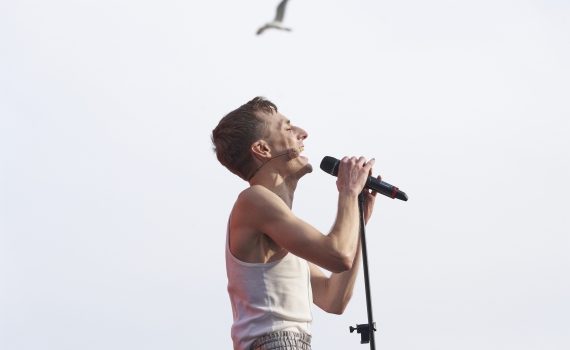 Razmus Nyström sjunger med en mikrofon. En fågel flyger ovanför honom