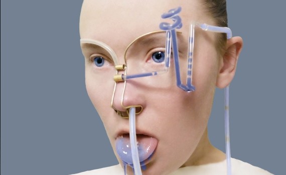 En kvinna med blå färg på tungan och en konstruktion med slangar och rör som går från näsan runt huvudet. 