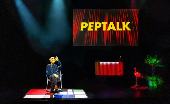 En docka på en scen med texten Peptalk bakom sig. 