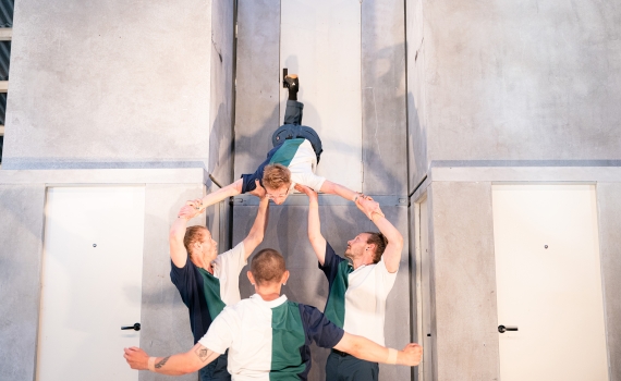 Fyra personer i blå, grön och vita tröjor utför akrobatik.