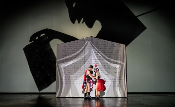 Två personer står framför en står bok på scenen i musikalen Matilda The Musical. 