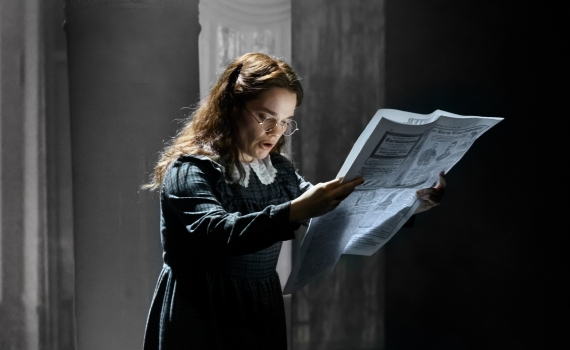 En skådespelare läser en tidning på scen i pjäsen Skuggan över stenbänken. 