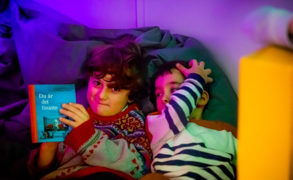 Två barn läser en bok i en kuddhörna
