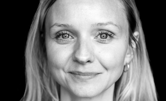 Kvinna i 30-årsåldern med långt blont hår och svart topp, fotograferad framifrån i svartvitt.