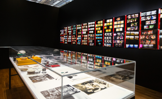 Monter med fotografiskt arbetsmaterial framför en vägg med kontaktkartor i färg.