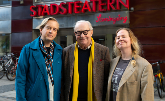 Tre personer framför Stadsteatern: man i blå rock, äldre man med glasögon och gul halsduk, kvinna i brun kavaj.