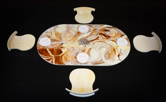 Ovalt bord med virvlande mönster, fyra stolar och fyra vita tallrikar, sett uppifrån.