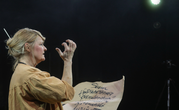 Åsa Gustafsson som håller ett stort papper i ena handen och en hand i luften.