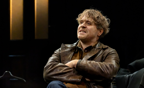 Yngre man med lockigt blont hår sitter med armarna i kors och ser åt sidan.