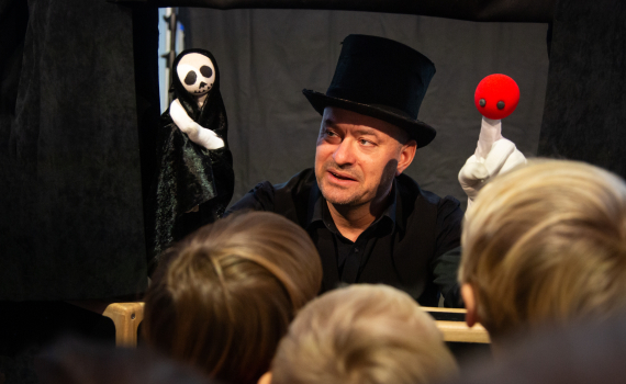 Man med hög hatt spelar dockteater för barn med handdockor.