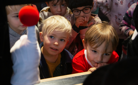 Flera barn tittar närbild på en röd handdocka under dockteater.