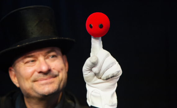 Närbild på man med hatt som håller upp röd docka med vita handskar.