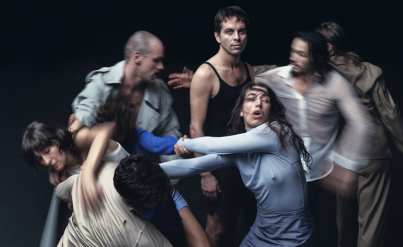 Sex vuxna dansare ca 20–40 i neutrala scenkläder drar och vrider varandras armar i dynamisk gruppkoreografi.