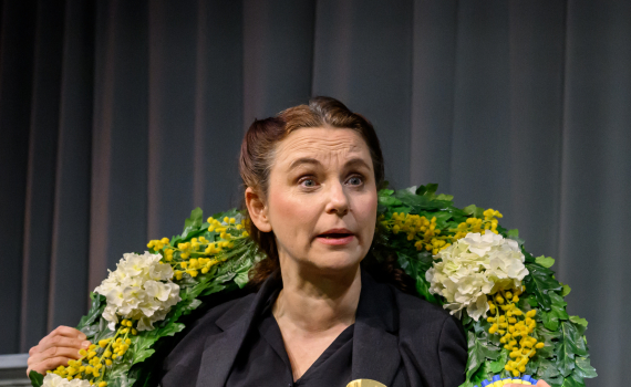 Anna Fahlstedt som Eva Hellstedt. Hon har en stor krans runt halsen.