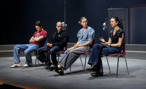 Fyra personer sitter på röda stolar på scen; ung kvinna i mörk topp gestikulerar medan hon talar.