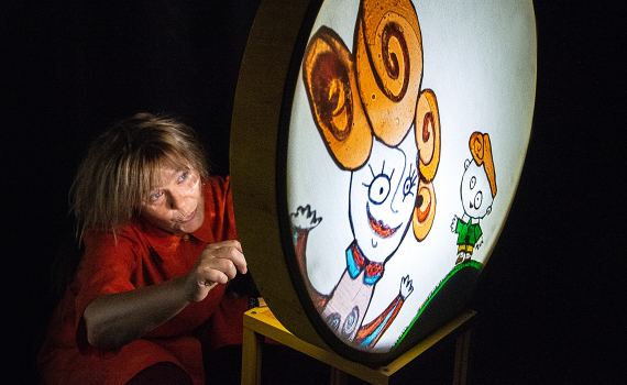 Person i röd klänning visar illustration på rund ljusskärm i mörk scenmiljö.